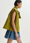 Woman wearing a green sleeveless top with a bow detail and a denim skirt on a white background