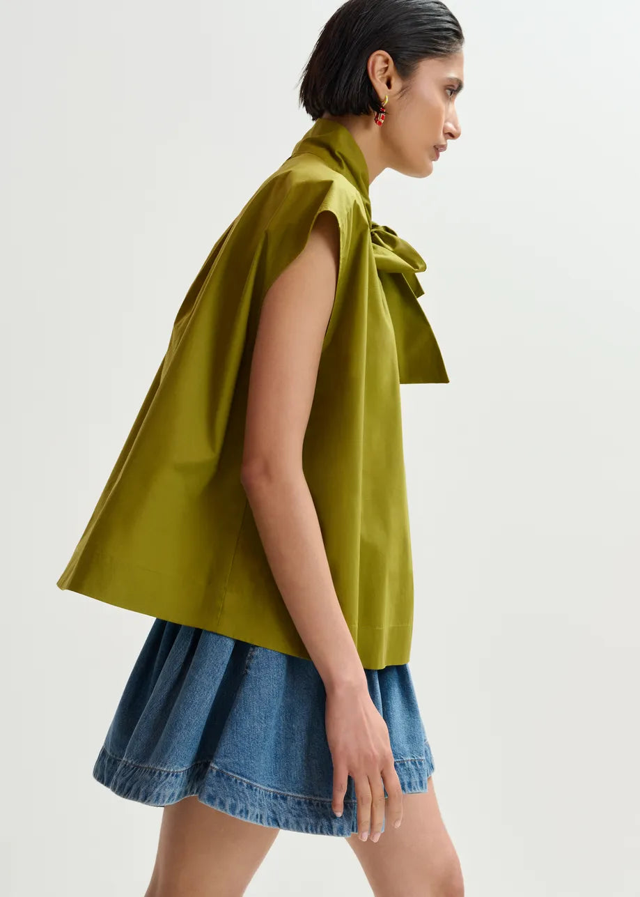 Woman wearing a green sleeveless top with a bow detail and a denim skirt on a white background