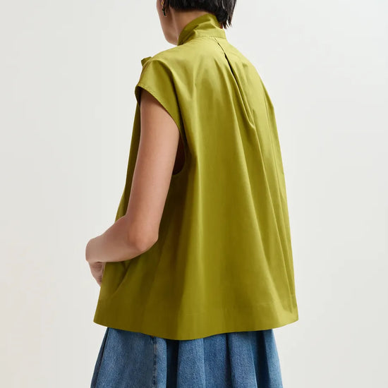 Person wearing a green sleeveless top and denim skirt on a white background