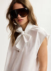 Woman wearing a white blouse with a bow and sunglasses on a plain background