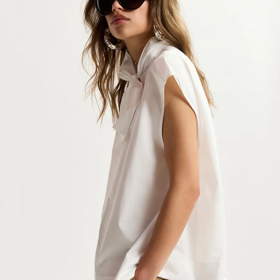 Woman wearing a white sleeveless top and sunglasses on a plain background