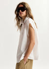 Woman wearing a white sleeveless top and sunglasses on a plain background