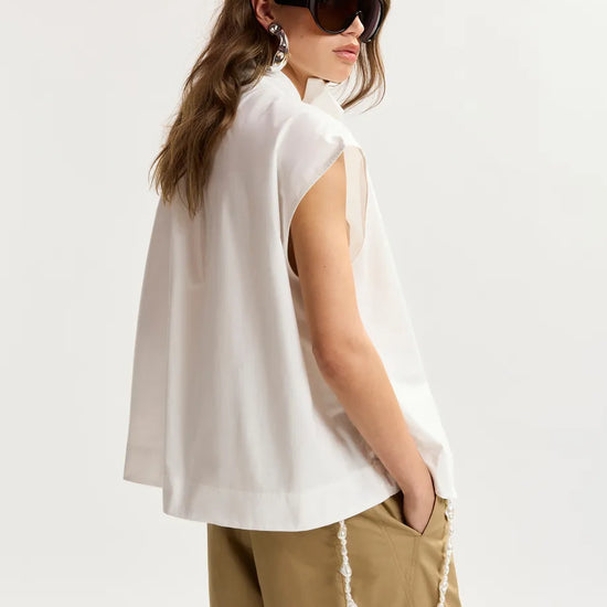 Woman wearing a white sleeveless top and beige pants on a plain background
