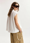 Woman wearing a white sleeveless top and beige pants on a plain background
