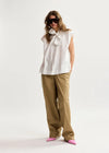 Woman wearing a white sleeveless top with a bow and beige pants on a white background
