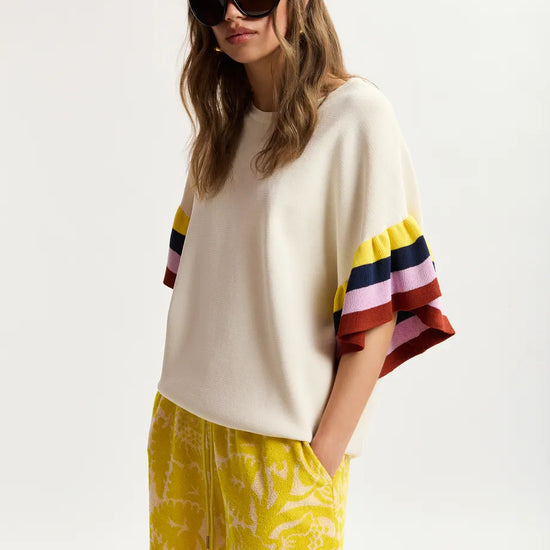 Woman wearing a white sweater with colorful sleeves and yellow shorts on a white background