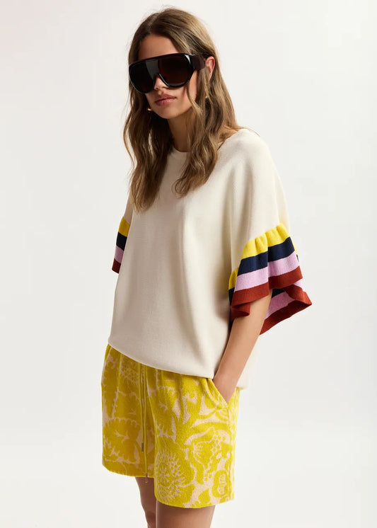 Woman wearing a white sweater with colorful sleeves and yellow shorts on a white background
