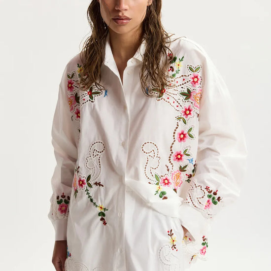 Woman wearing a white embroidered shirt on a plain background