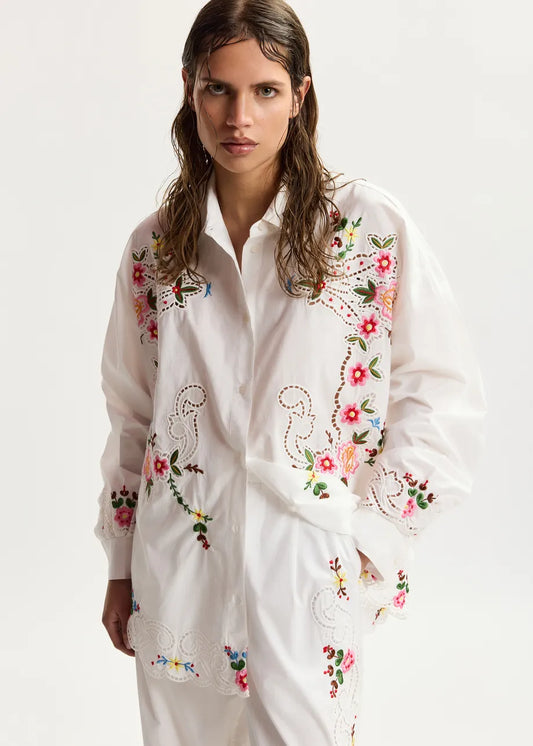 Woman wearing a white embroidered shirt on a plain background