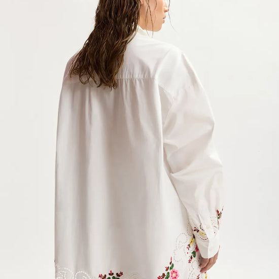 Woman wearing a white blouse with floral embroidery on a plain background