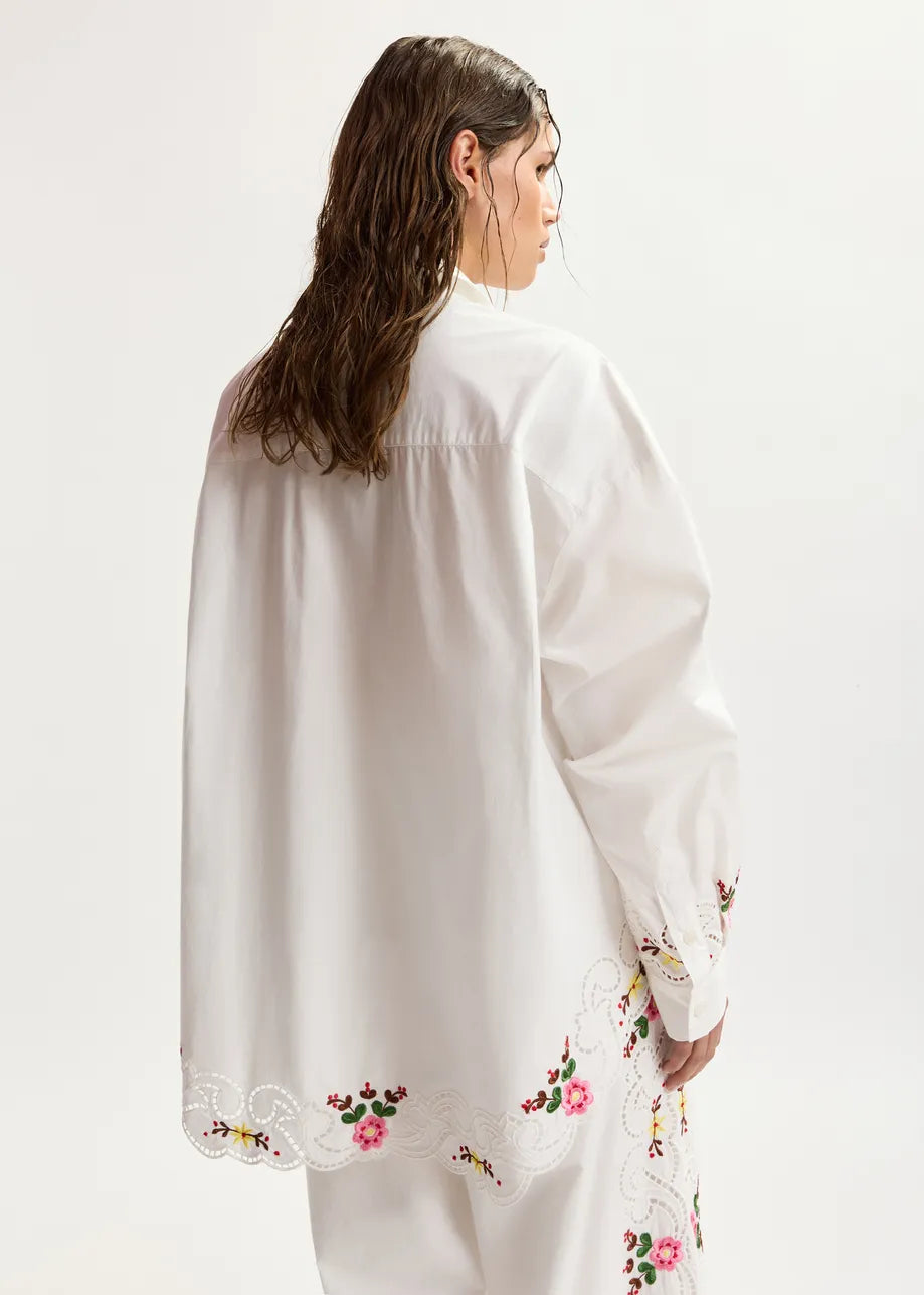 Woman wearing a white blouse with floral embroidery on a plain background
