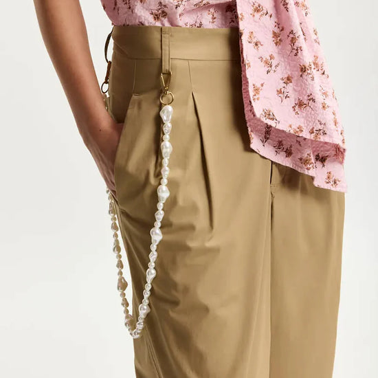 Person wearing beige pants with a pink floral top on a white background