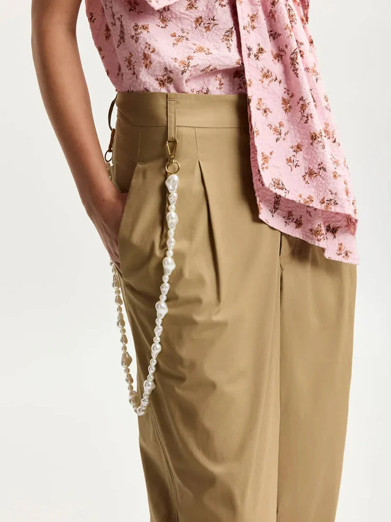 Person wearing beige pants with a pink floral top on a white background