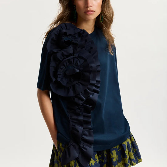 Woman wearing a navy blue top with ruffles and a patterned skirt on a white background