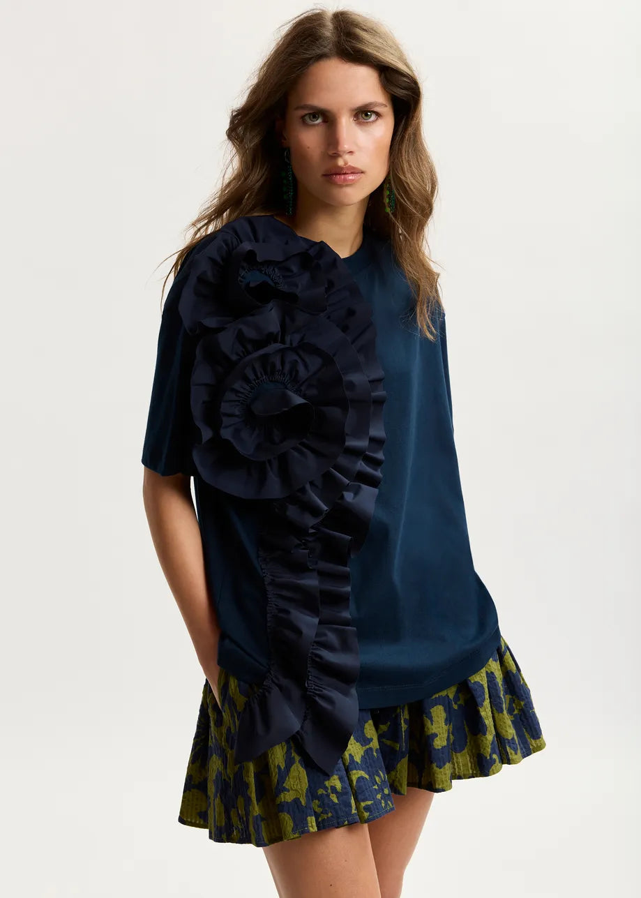 Woman wearing a navy blue top with ruffles and a patterned skirt on a white background