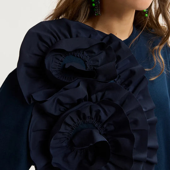 Navy blue blouse with ruffled details worn by a person on a light gray background