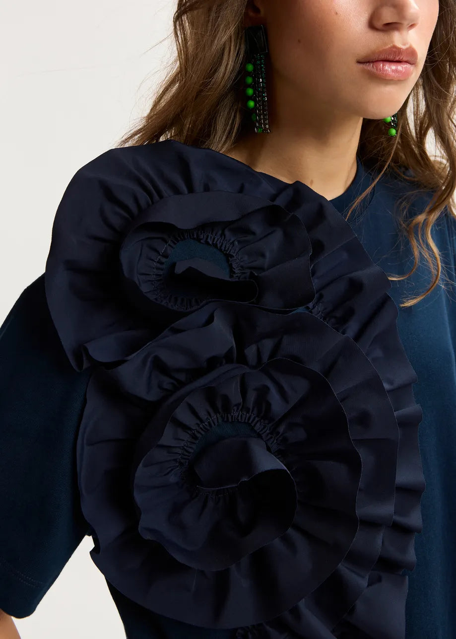 Navy blue blouse with ruffled details worn by a person on a light gray background