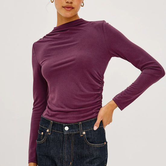 model sown wearing a burgundy mock neck long sleeve top on a grey bakground