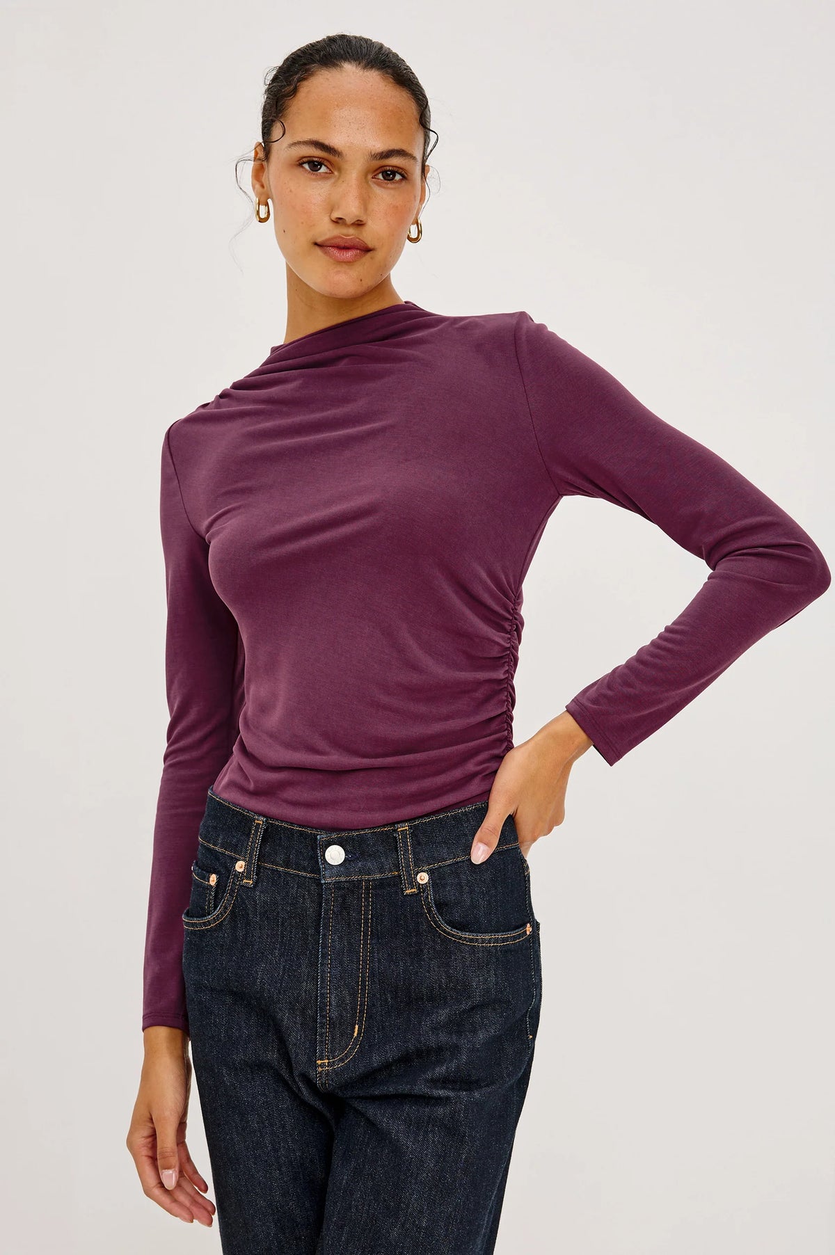 model sown wearing a burgundy mock neck long sleeve top on a grey bakground