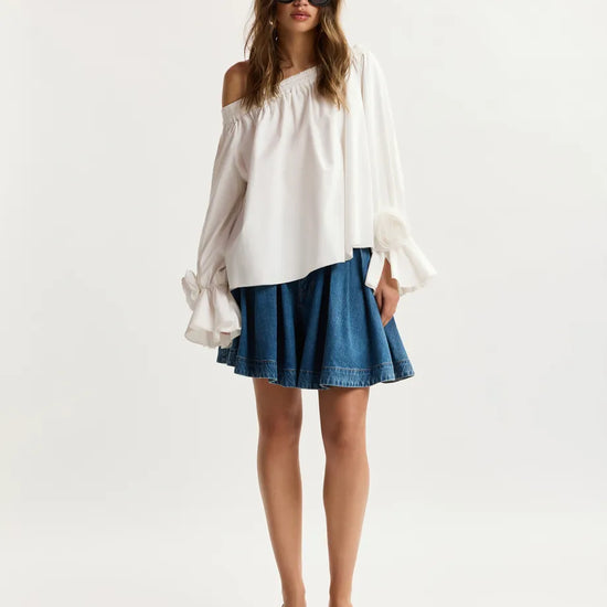 Woman wearing a white off-shoulder top and blue denim skirt on a white background