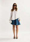 Woman wearing a white off-shoulder top and blue denim skirt on a white background