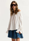Woman wearing a white off-shoulder top and blue denim skirt on a white background