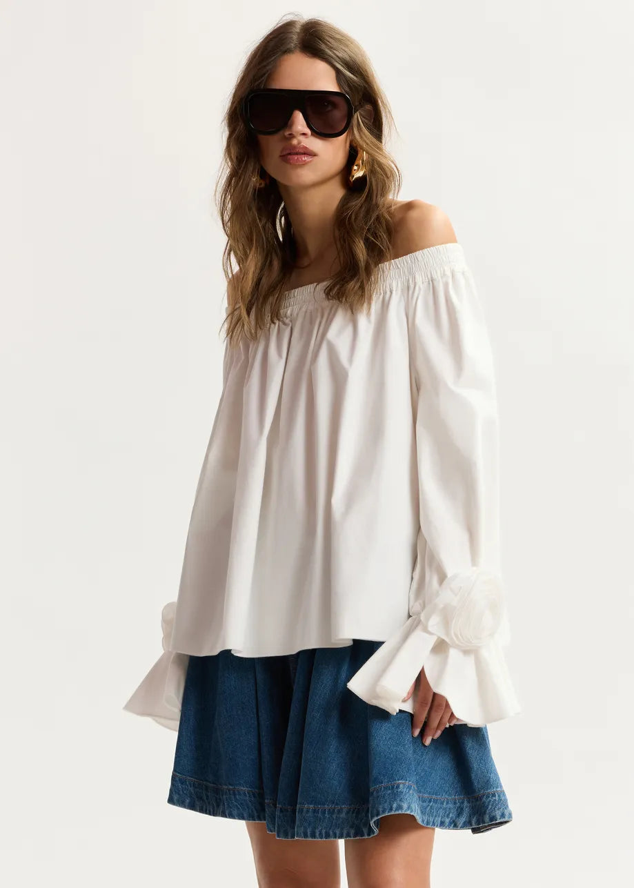 Woman wearing a white off-shoulder top and blue denim skirt on a white background
