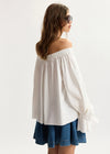 Woman wearing a white off-shoulder top and denim skirt on a plain background