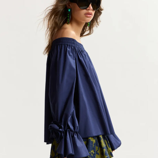 Woman wearing a blue off-shoulder top and patterned shorts on a white background