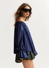Woman wearing a blue off-shoulder top and patterned shorts on a white background