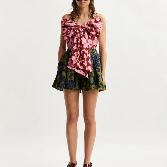 Woman wearing a floral top and shorts with sunglasses on a white background