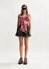 Woman wearing a floral top and shorts with sunglasses on a white background