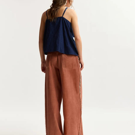 Woman wearing a navy top and brown pants on a white background