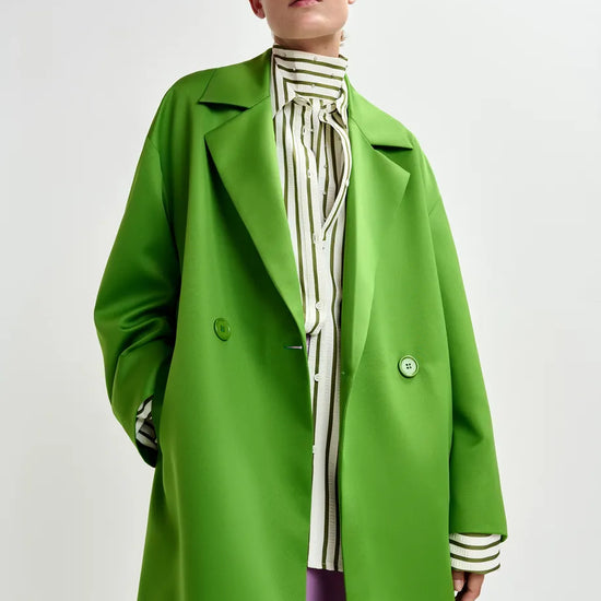 Person wearing a bright green coat over a striped shirt on a white background