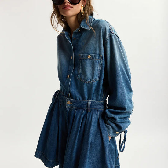 Woman wearing a blue denim dress with sunglasses on a white background