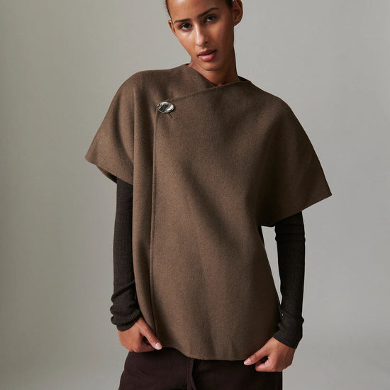 Person wearing a brown poncho over a dark long-sleeve shirt and pants on a neutral background