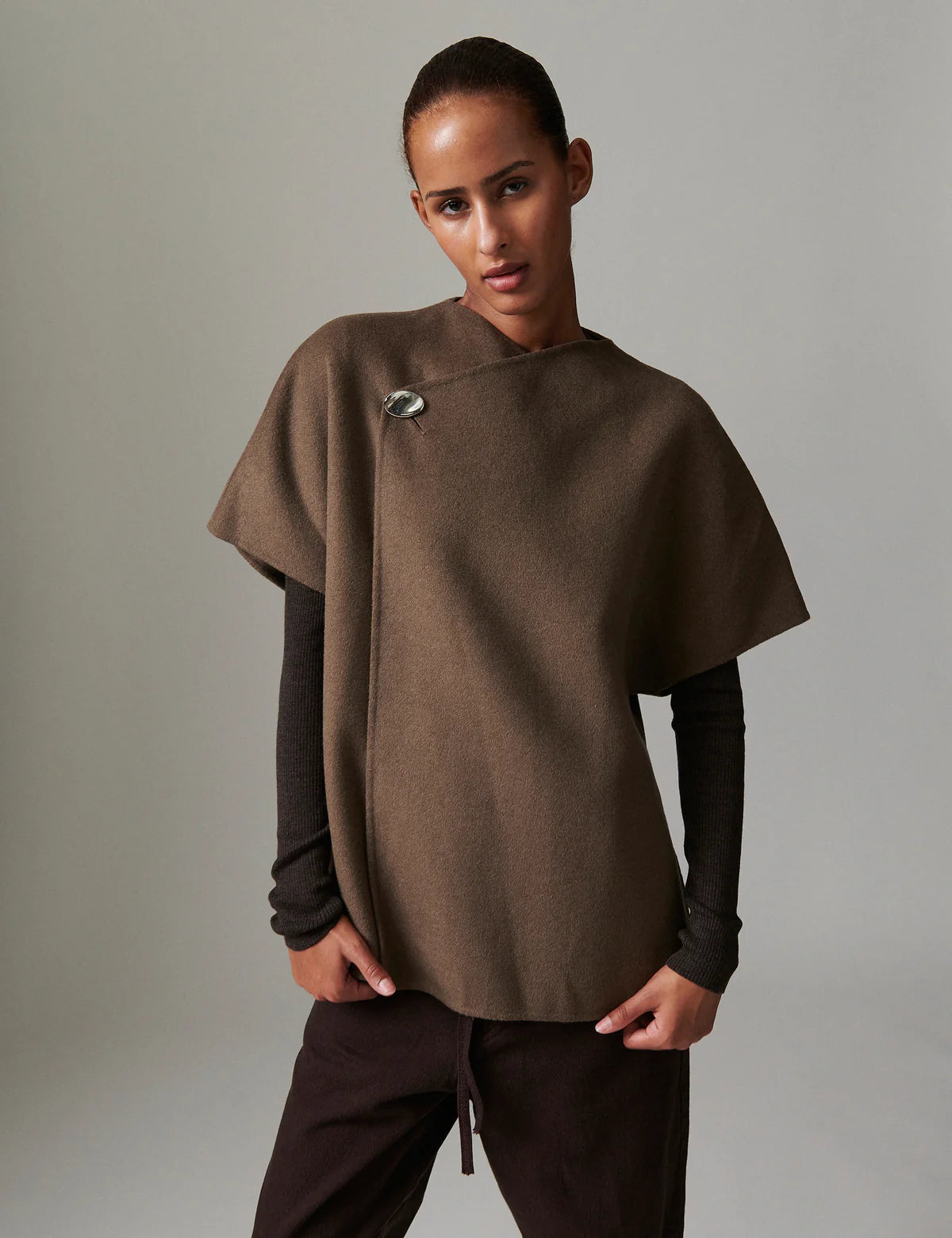 Person wearing a brown poncho over a dark long-sleeve shirt and pants on a neutral background