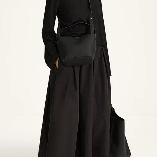 A model wearing a black long-sleeve maxi dress with a matching black crossbody bag and brown strappy sandals, photographed against a clean white studio background.