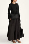 A model wearing a black long-sleeve maxi dress with a matching black crossbody bag and brown strappy sandals, photographed against a clean white studio background.