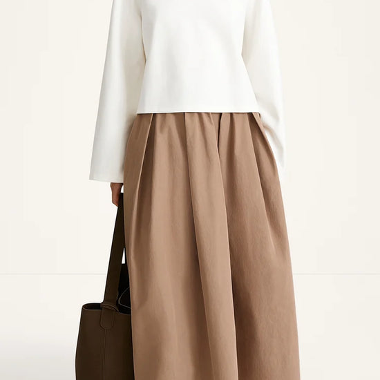 Woman wearing a white top and brown skirt with a brown bag on a white background