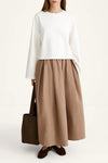 Woman wearing a white top and brown skirt with a brown bag on a white background