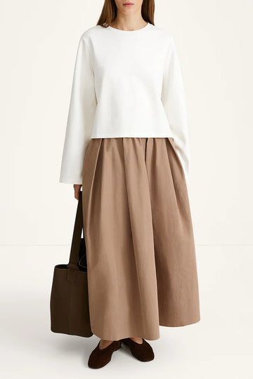 Woman wearing a white top and brown skirt with a brown bag on a white background