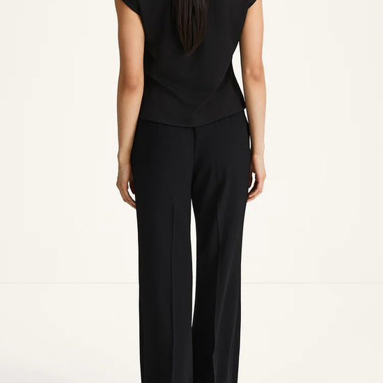 A woman viewed from the back wearing a black sleeveless top and matching black wide-leg trousers against a plain light background.