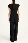 A woman viewed from the back wearing a black sleeveless top and matching black wide-leg trousers against a plain light background.