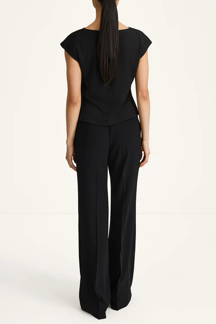 A woman viewed from the back wearing a black sleeveless top and matching black wide-leg trousers against a plain light background.