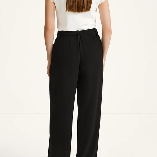 A woman shown from the back wearing black wide-leg trousers and a white short-sleeve top against a plain light background.