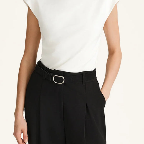 Person wearing a white sleeveless top and black pants on a plain background
