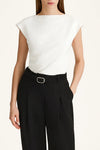 Person wearing a white sleeveless top and black pants on a plain background