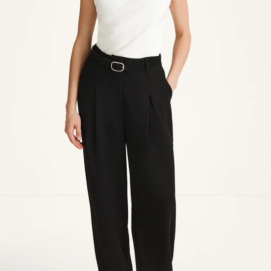 A model wearing black wide-leg trousers with a matching black belt and silver buckle, paired with a white sleeveless top and black sandals, against a plain white studio background.