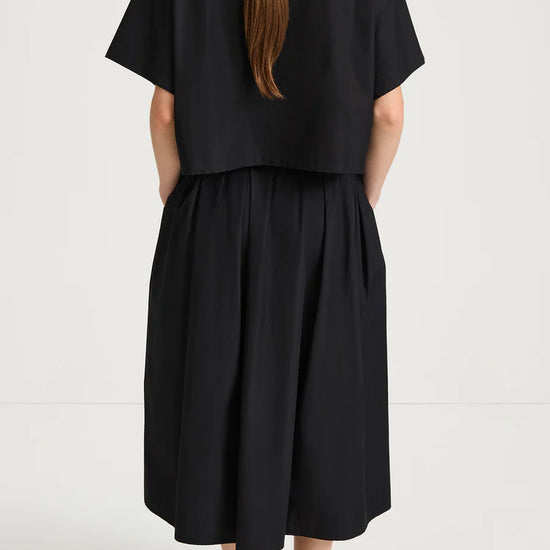 Person wearing a black top and skirt with a plain background rear view